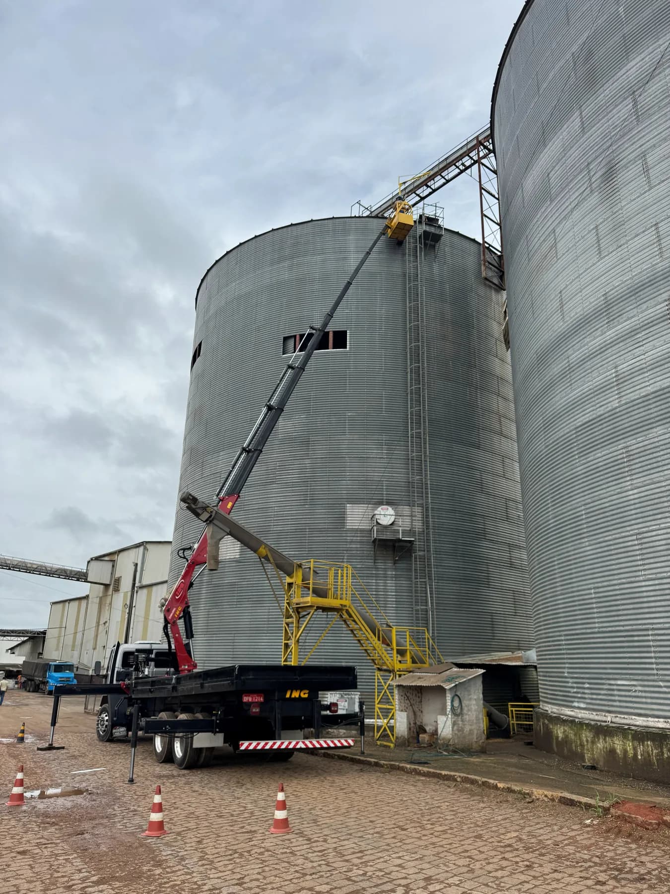 Lança do munck totalmente estendida levando um trabalhador em cesto aéreo até o topo de um silo graneleiro metálico