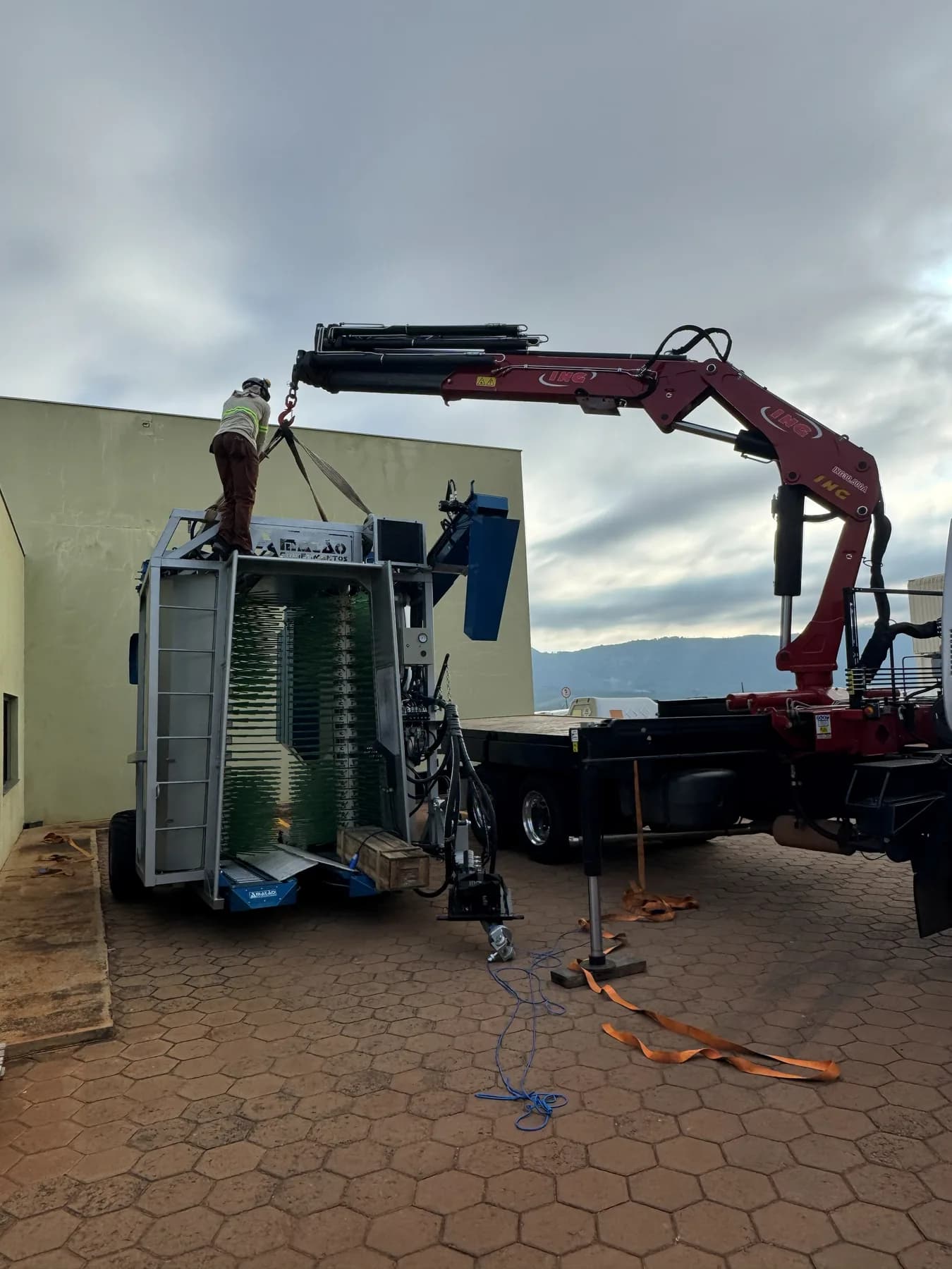 Operador de colete refletivo conferindo as cintas de içamento sobre uma máquina agrícola antes de o munck levantá-la