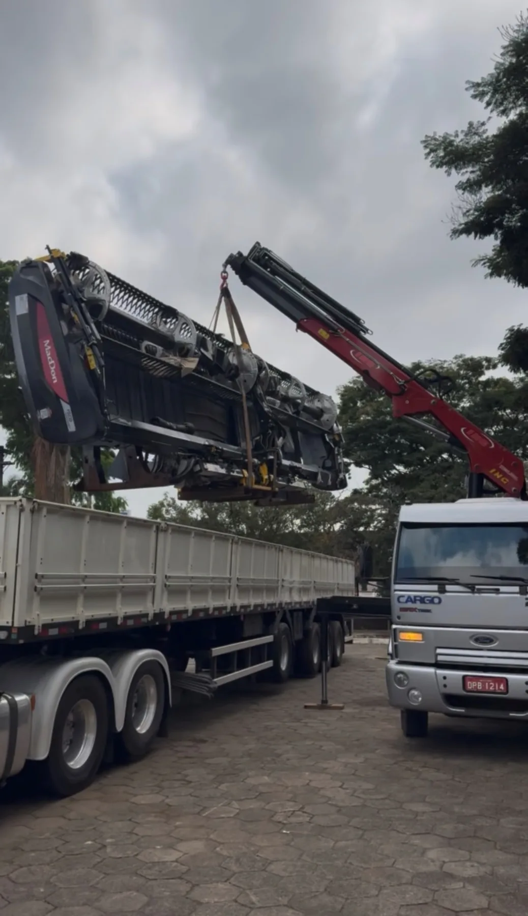 Munck içando uma plataforma de corte MacDon suspensa por cintas acima da carroceria de uma carreta