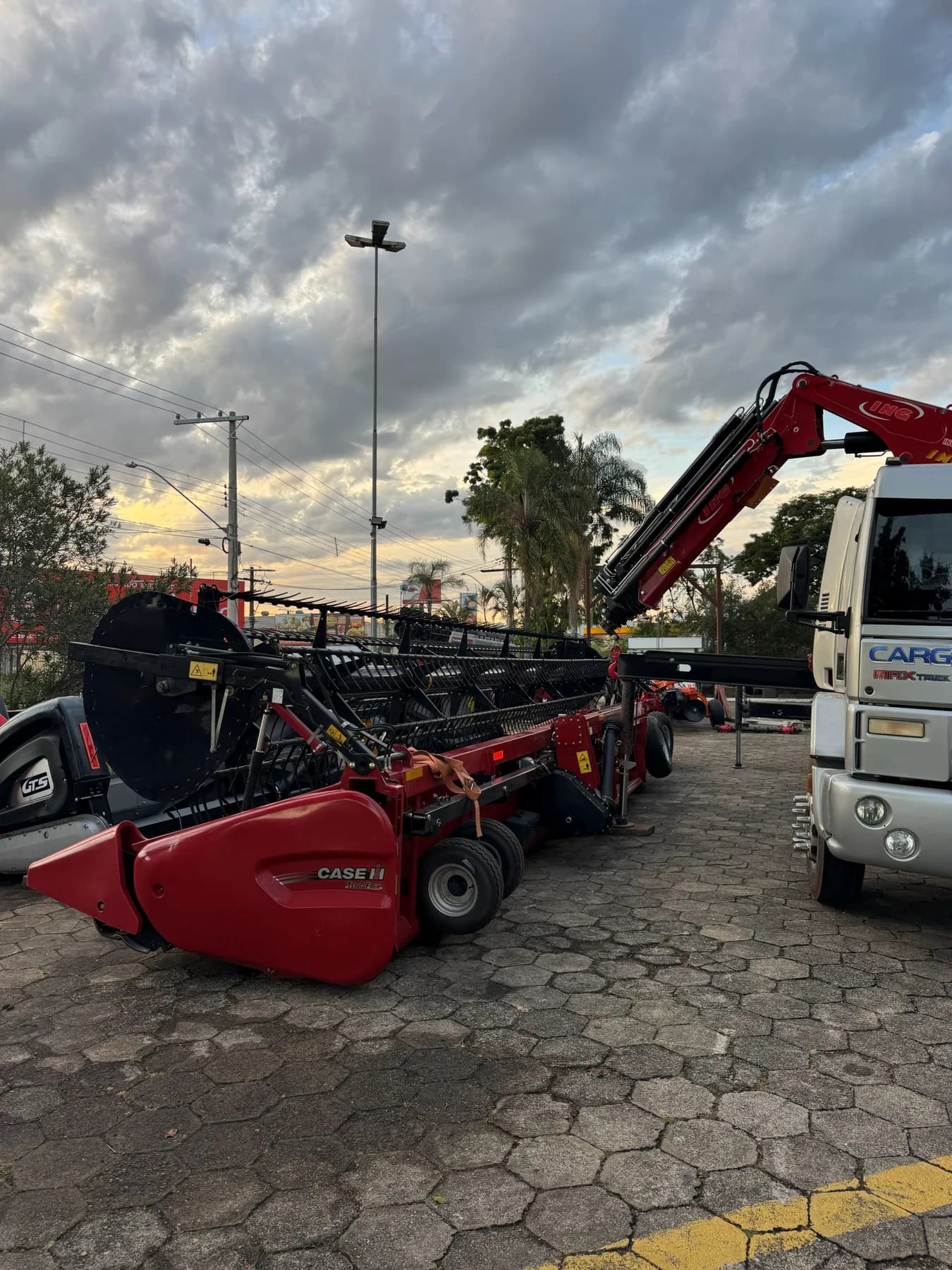 Plataforma de corte de colheitadeira CASE IH estacionada ao lado do caminhão munck no fim da tarde